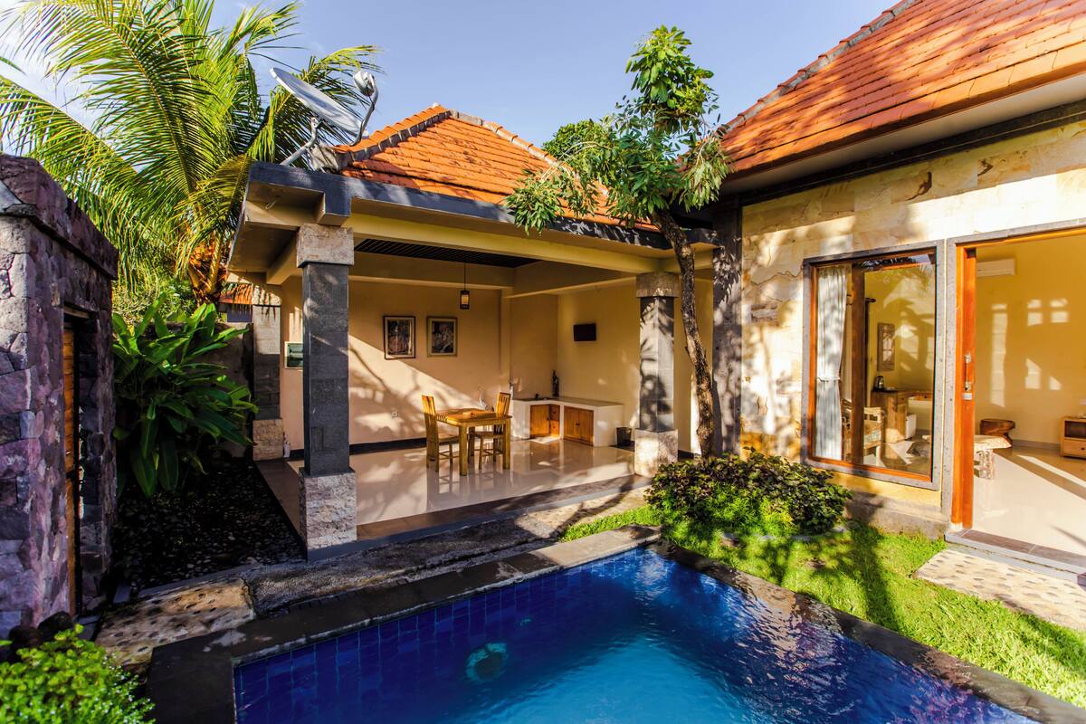 Uma área à beira da piscina com uma piscina revestida, um espaço de estar coberto e uma parede de pedra.