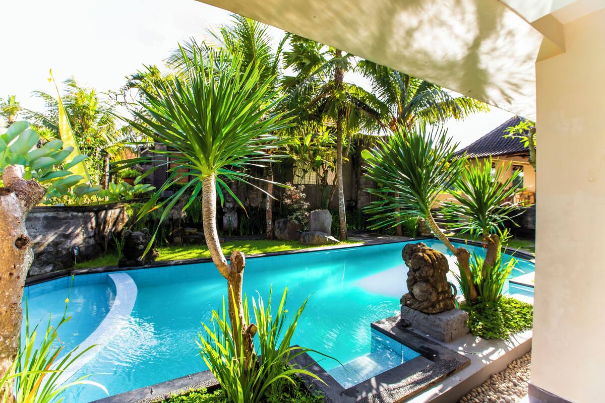 Uma piscina rodeada por plantas tropicais e uma estátua de pedra.