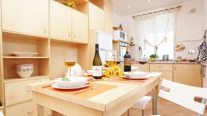 A dining area with a wooden table set for two, a bottle of wine, and a bottle of olive oil.