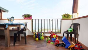 A balcony with a dining table, chairs, children's toys, and potted plants.