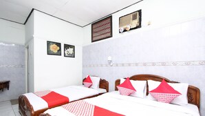 A hotel room with two wooden beds, white and red bedding, a wall-mounted air conditioner, and a decorative wall panel.