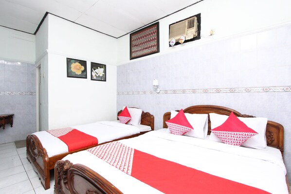 A hotel room with two wooden beds, white and red bedding, a wall-mounted air conditioner, and a decorative wall panel.