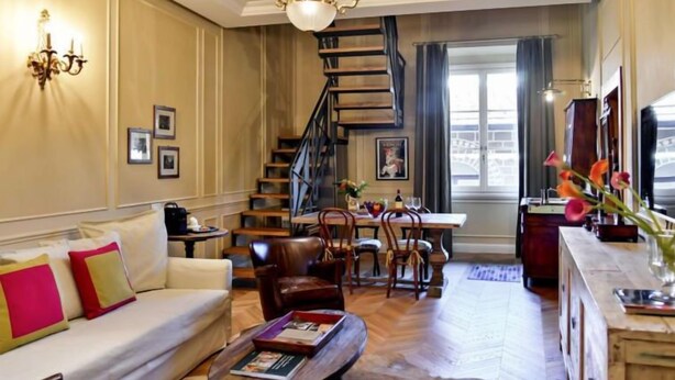 Ein geräumiges Wohnzimmer mit einer Couch, einem Couchtisch und einem Essbereich mit Stühlen. Eine Treppe führt zu einer weiteren Ebene.