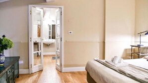 Ein Schlafzimmer mit einem Bett, einem Schreibtisch, einem Stuhl und einer Kommode. Eine Tür führt zu einem Badezimmer.