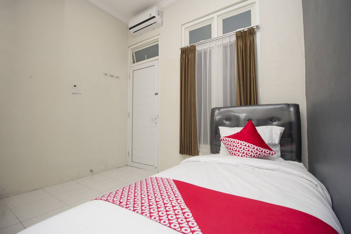 Una habitación de hotel con cama, ventana con cortinas, aire acondicionado y una puerta.