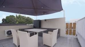 Une terrasse extérieure avec une table et des chaises, un grand parasol et un appareil de climatisation.
