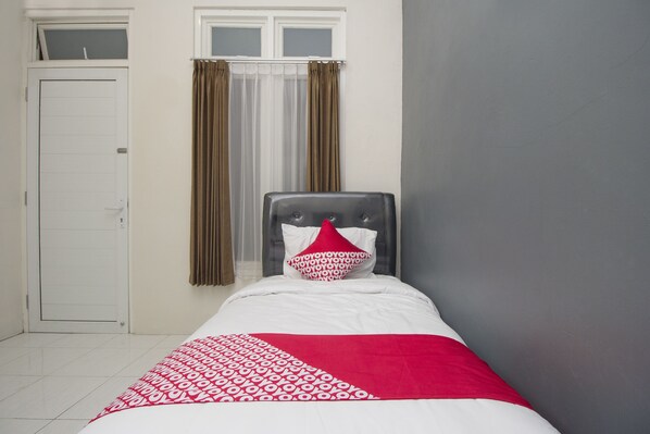 Un lit simple avec une couvre-lit à motifs, une tête de lit et une fenêtre avec des rideaux.