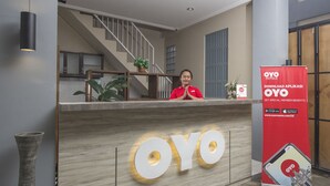 Un comptoir d’accueil avec un grand panneau lumineux portant l’inscription « OYO », un escalier en arrière-plan et une banderole promotionnelle pour l’application OYO.