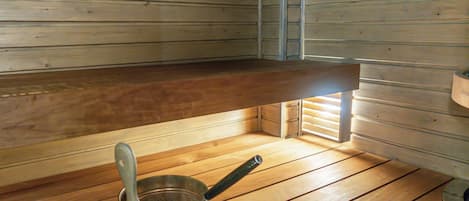 A wooden interior with a bench, a metal pot with a spoon, and a window.