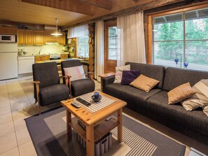 Een gezellige woonkamer met een bank, stoelen, een salontafel en een keuken op de achtergrond.
