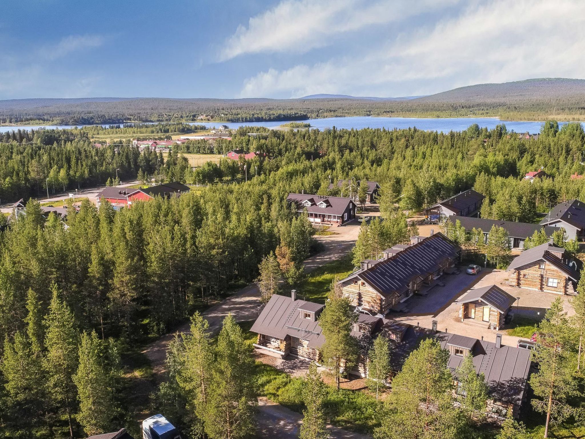 A residential area with multiple houses surrounded by dense forests and a lake in the background.