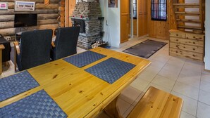 A wooden dining table with four black placemats, a stone fireplace, and a wooden staircase.