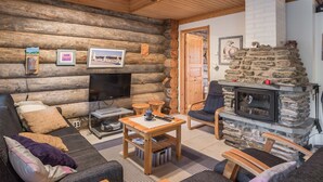 A cozy log cabin interior with a stone fireplace, a television, and a comfortable seating area.