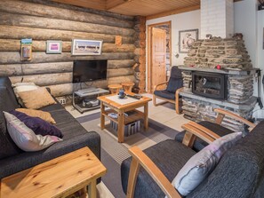 Een interieur van een blokhut met een bank, stoelen, een salontafel, een open haard en een televisie.