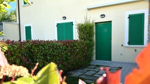 Ein Gebäude mit grüner Tür, grünen Fensterläden und einem kleinen Garten mit Pflanzen und einem Steinweg.