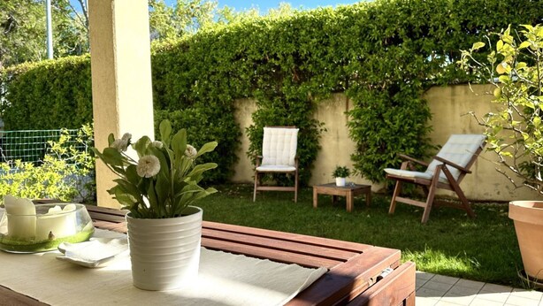 Eine Terrasse mit einem Holztisch, einem Blumentopf und zwei weißen Stühlen.