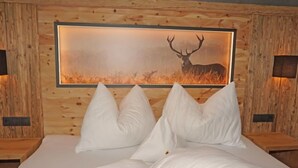 Un letto con biancheria e cuscini bianchi, un quadro con corna di cervo appese al muro e rivestimento in legno.