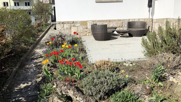 Un jardin avec un chemin de pierres, du mobilier d’extérieur et une variété de fleurs.