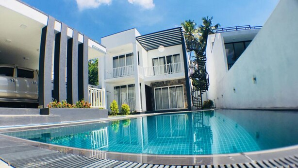 A modern pool area with a clear blue pool, a covered seating area, and a staircase leading to a second floor. - Royal Mansions Grand Luxury Villas (Kandy)