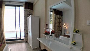 A hotel room with a large mirror, a white wardrobe, a bedside table with a vase of flowers, and a view of the outdoors through a sliding door. - Royal Mansions Grand Luxury Villas (Kandy)