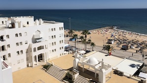 Un hotel costero con terraza en la azotea, una playa con sombrillas y una vista despejada del mar.