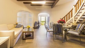 A spacious living room with a sofa, coffee table, and striped chairs. A staircase with wooden railings leads to an upper level. - El Dorado Playa - Villa La Roca by Interhome (Cambrils)