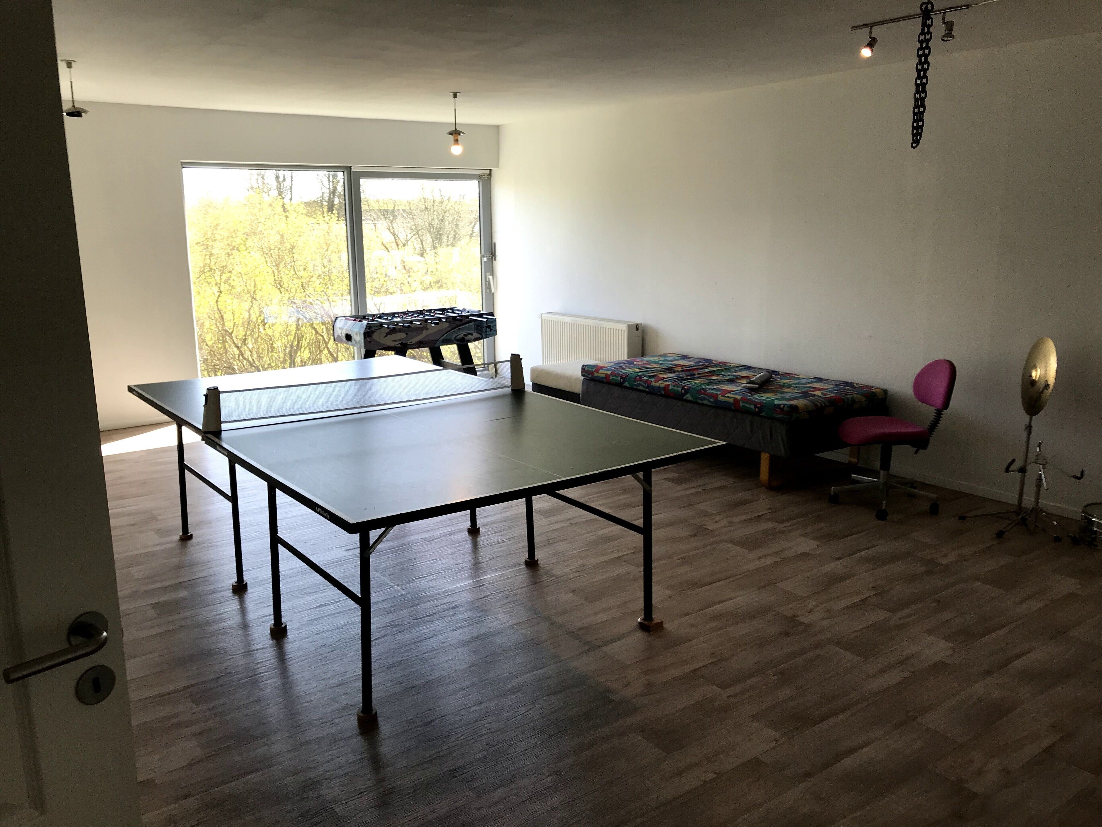 A room with a ping pong table, a sofa, a chair, and a drum set.