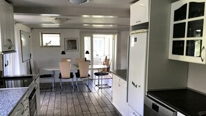A kitchen with white cabinets, a dining area with chairs, and a refrigerator. - In nature, close to the city (Aabenraa)
