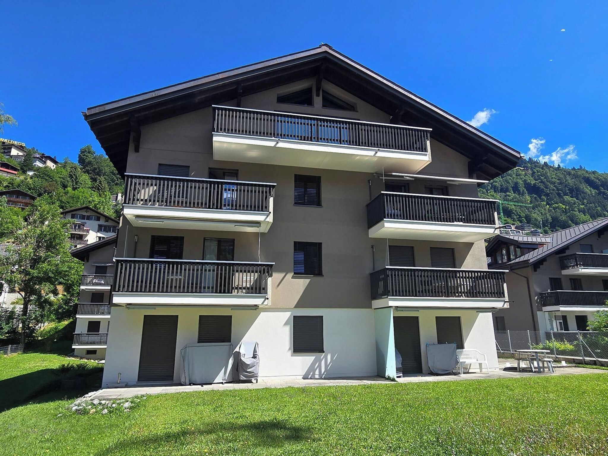 A multi-story building with balconies, a flat roof, and a grassy front yard.