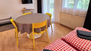 Habitació amb taula rodona, cadiretes grogues, televisió de pantalla plana, radiador i finestra amb cortines.