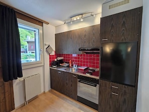 Une cuisine moderne avec des meubles en bois foncé, un réfrigérateur en acier inoxydable, un four encastré et un dosseret de crédence en carreaux rouges.
