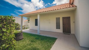 A building with a tiled roof, a covered walkway, and a well-maintained lawn. - Slowing Villas - Villa Oceano (Porto Santo)