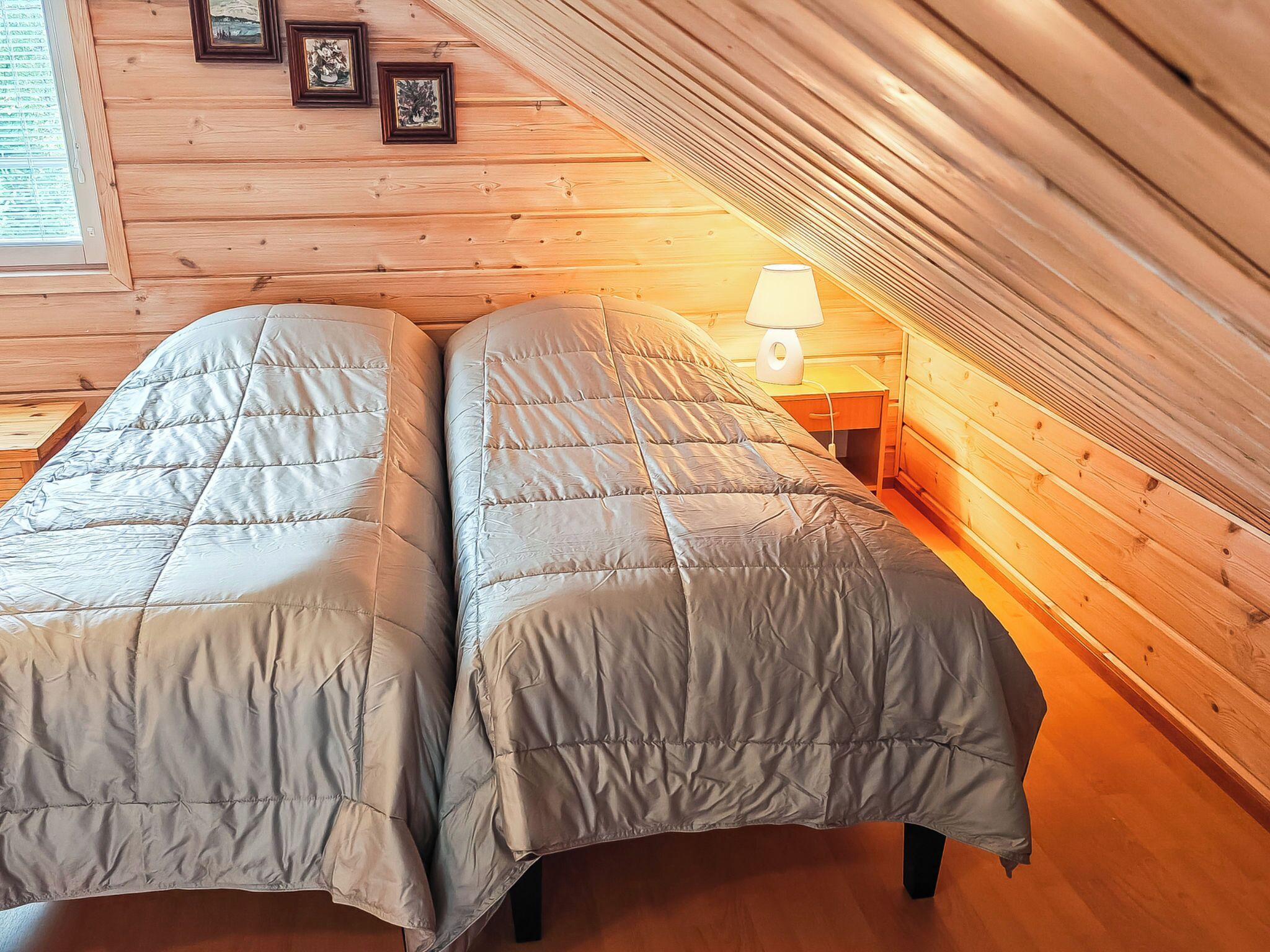 A room with two beds, a wooden ceiling, and a nightstand with a lamp.