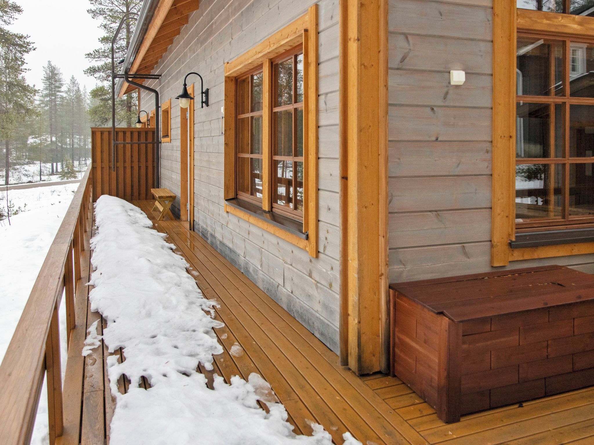 A wooden cabin with a deck, large windows, and a bench.