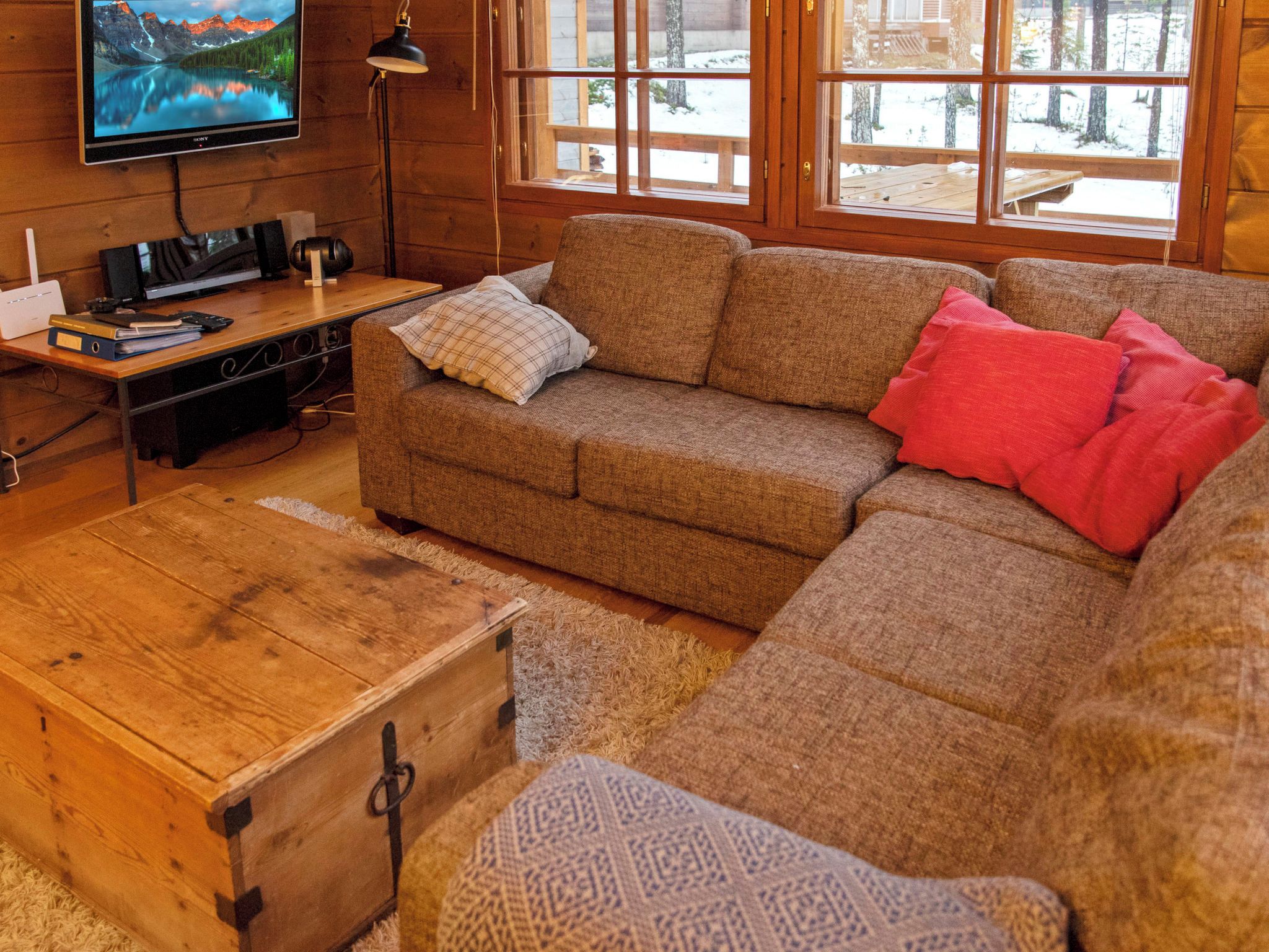 Een gezellige woonkamer met een houten vloer, een bank, een televisie en een houten kist.