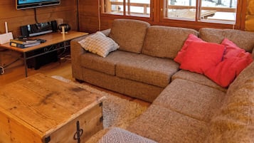 Ein gemütliches Wohnzimmer mit Holzboden, einer Couch, einem Fernseher und einer Holzkommode.
