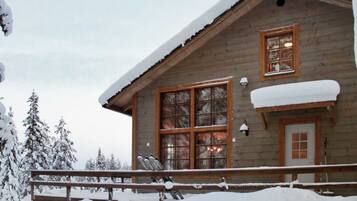 Une cabane en bois avec une grande fenêtre, une porte et un toit recouvert de neige.