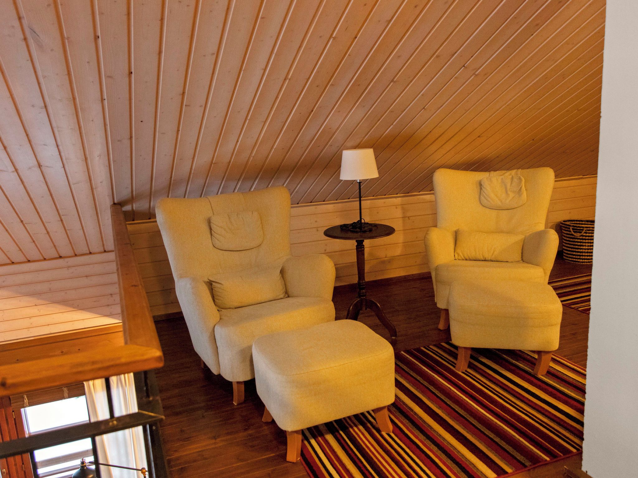 A cozy room with two armchairs and a small table, wooden slatted ceiling, and a striped rug.