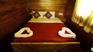 A wooden cabin-style room with a bed, two decorative pillows, a red bedspread, and two towels arranged on the bed. - Hiliya Resort - Hostel (Sulthan Bathery)