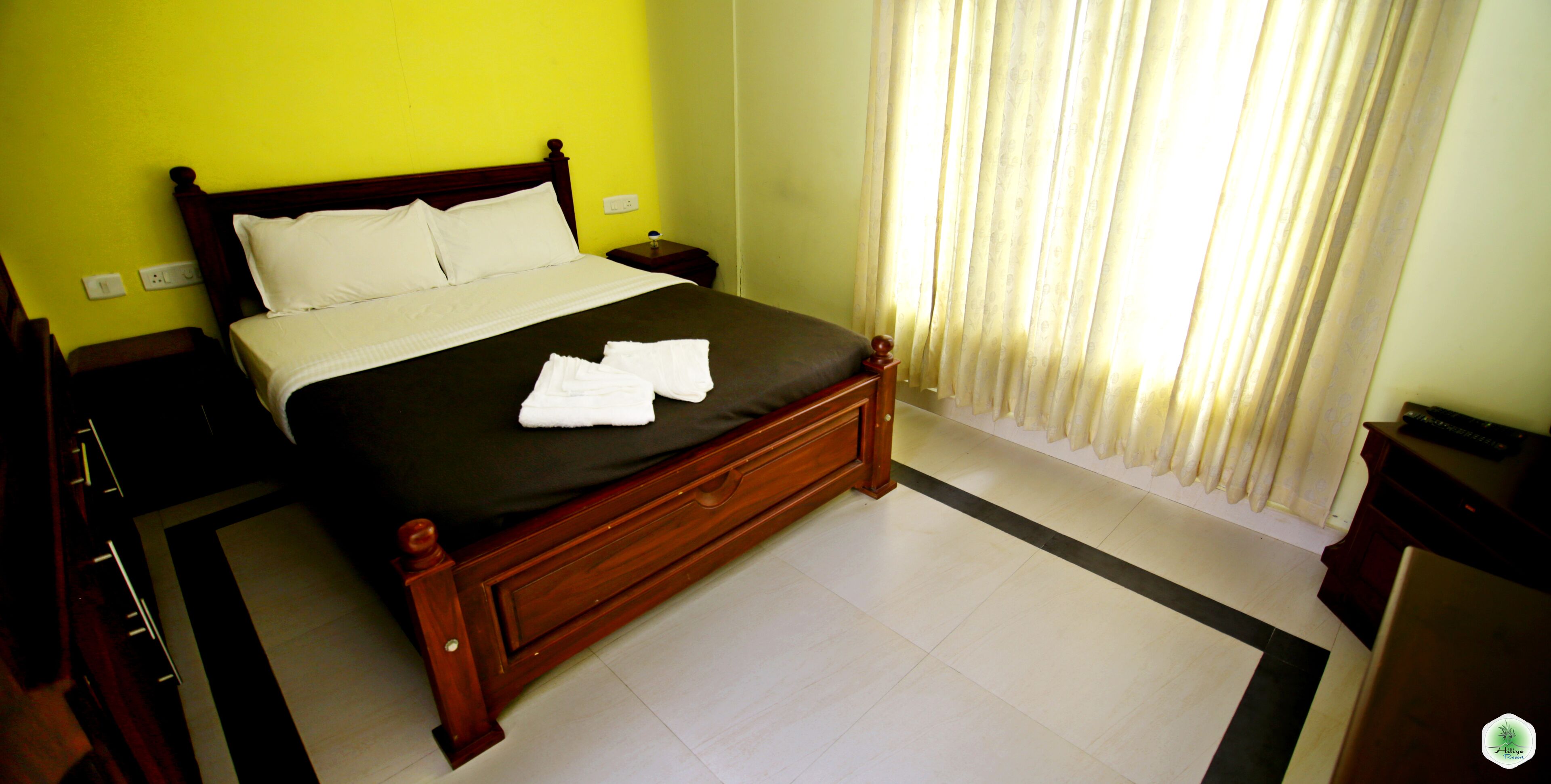 A neatly made bed with white linens and towels, a wooden headboard, and a nightstand with a lamp.