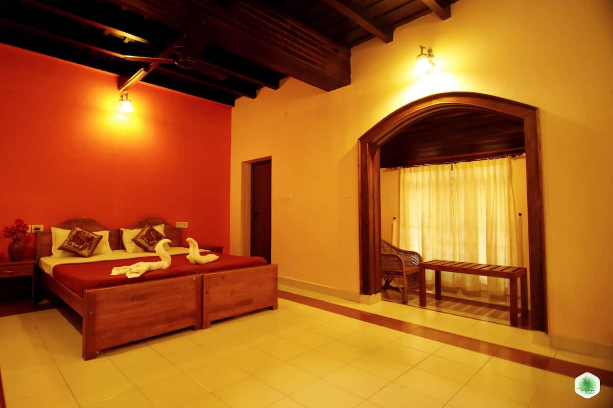 A room with a wooden bed, a small table, and a chair. There is a door and a window with curtains.