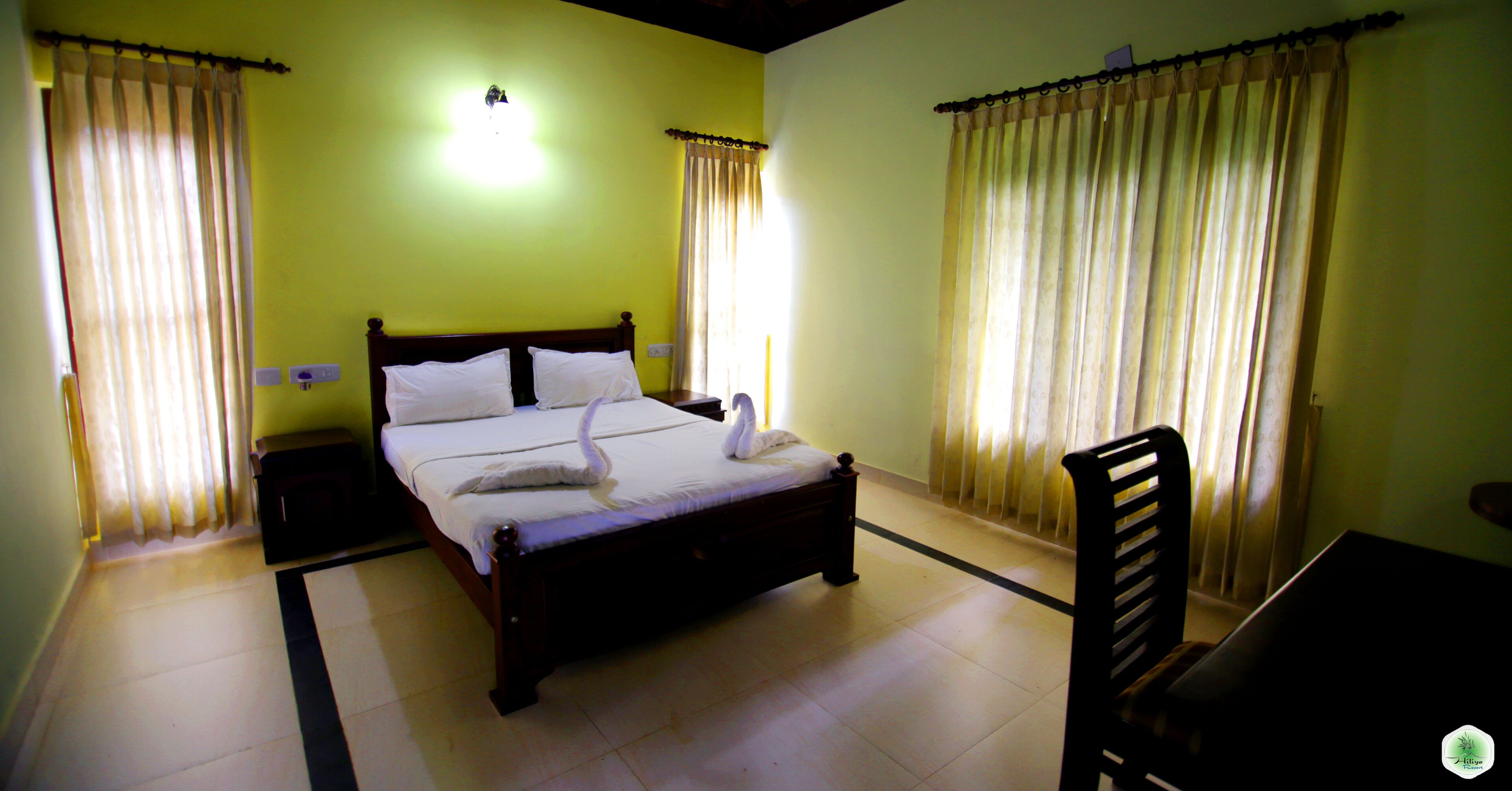 Una habitación de hotel con una cama, mesitas de noche, una silla y cortinas.
