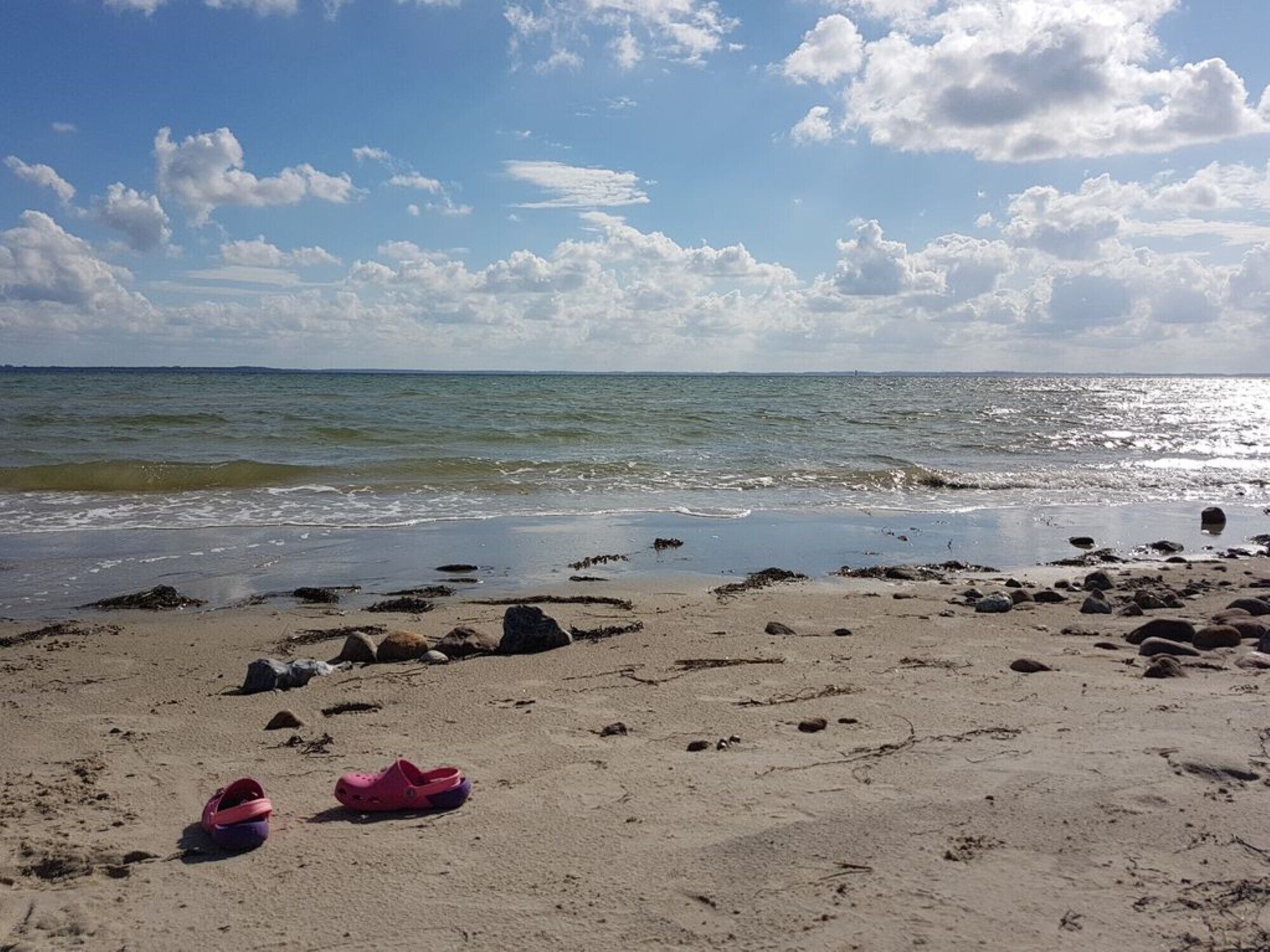 Una playa con arena, rocas y un par de sandalias rosas.