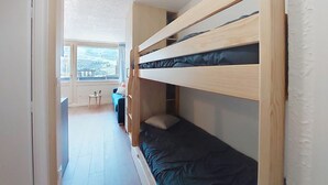 A compact room with a bunk bed, a small table, and a view of a balcony. - Aravis 314 by Interhome (Les Menuires)