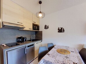 A compact kitchen with a microwave, coffee maker, and dishwasher. There is a dining table with chairs and a decorative wall piece. - Aravis 314 by Interhome (Les Menuires)