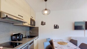 Une cuisine compacte équipée d’un four à micro-ondes, d’une machine à café et d’un luminaire suspendu moderne.