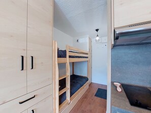 Una habitación pequeña con literas, kitchenette y un mueble con cajones.