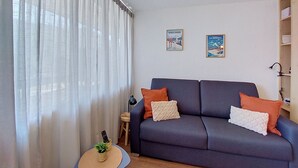 Un salon avec un canapé bleu foncé, deux coussins, une petite table ronde ornée d’une plante, et deux affiches encadrées accrochées au mur.