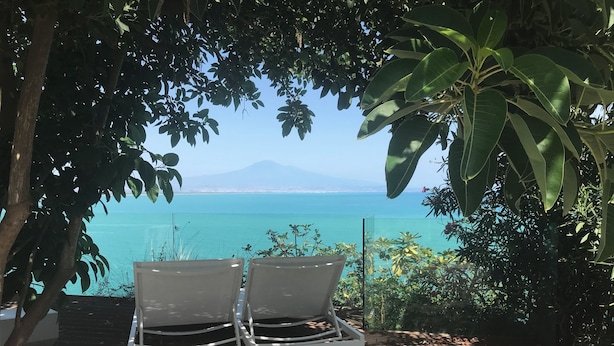 A view of a coastal area with a clear blue sea, a distant mountain, and a seating area with two chairs under a tree. - New terrace sea view villa (Augusta)