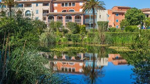 A hotel with multiple stories, balconies, and a reflection in a pond.